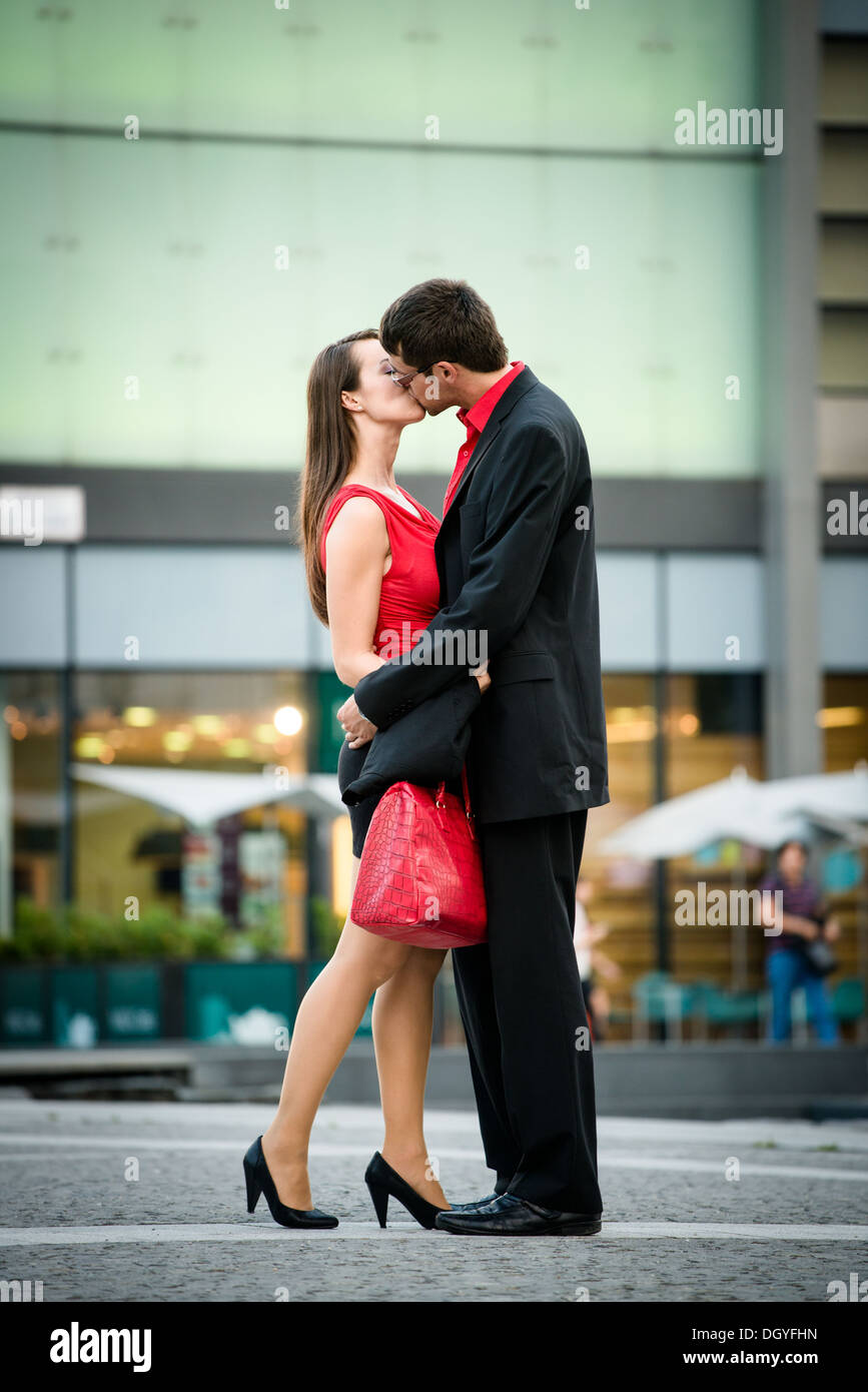 Young business couple dressed in red kiss and welcome each other on street Stock Photo