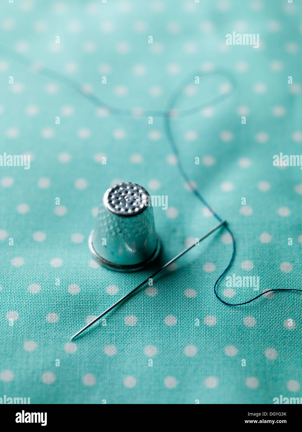 A threaded needle and thimble on top of polka dotted fabric Stock Photo