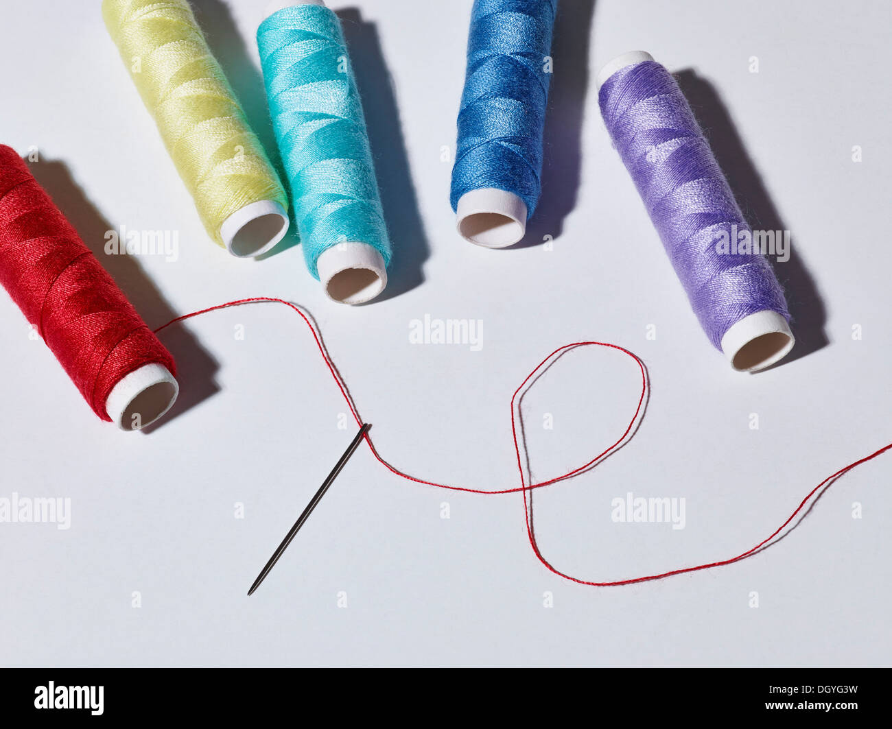A threaded needle lying below five spools of different colored thread Stock Photo