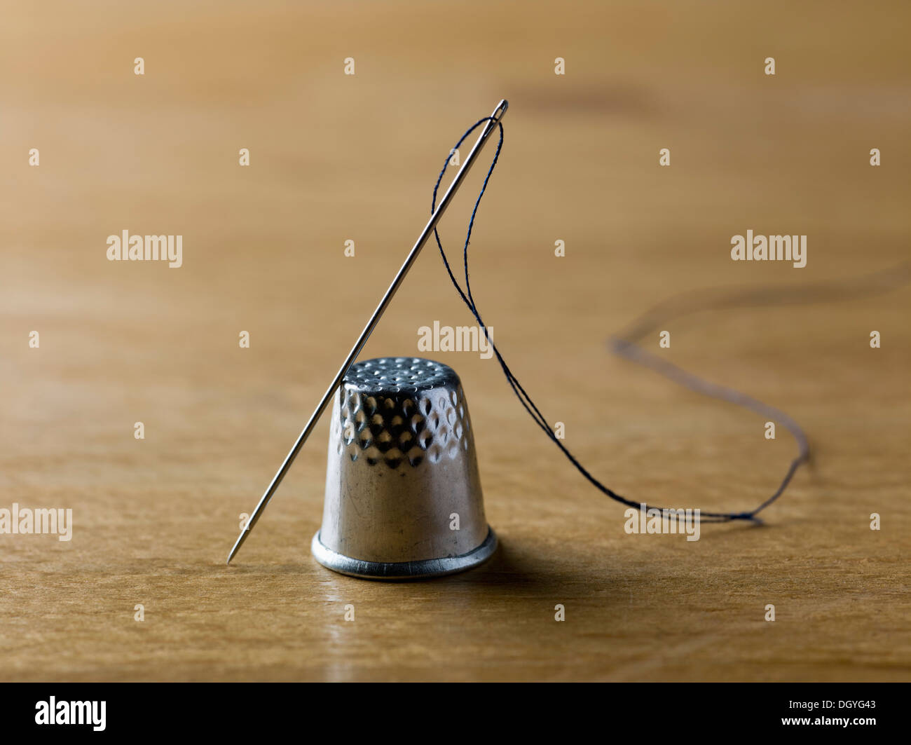 A threaded needle balanced against a shiny metal thimble Stock Photo