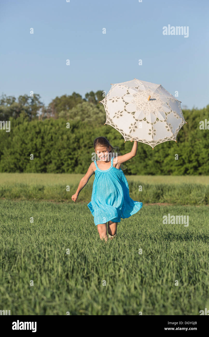 A young girl holding an umbrella up while running through a field in summer Stock Photo