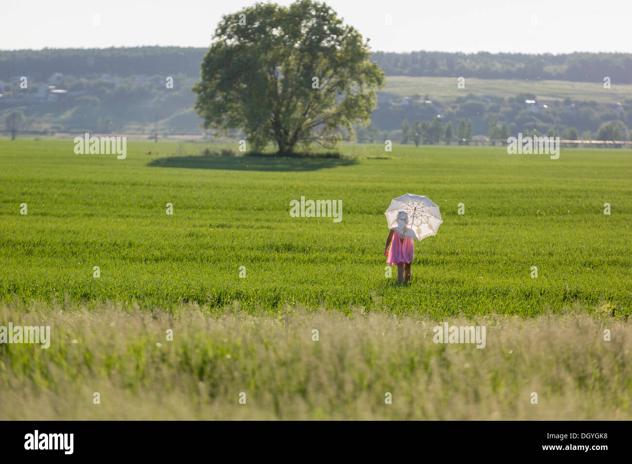 A young girl walking through a field using an umbrella as protection against the sun Stock Photo