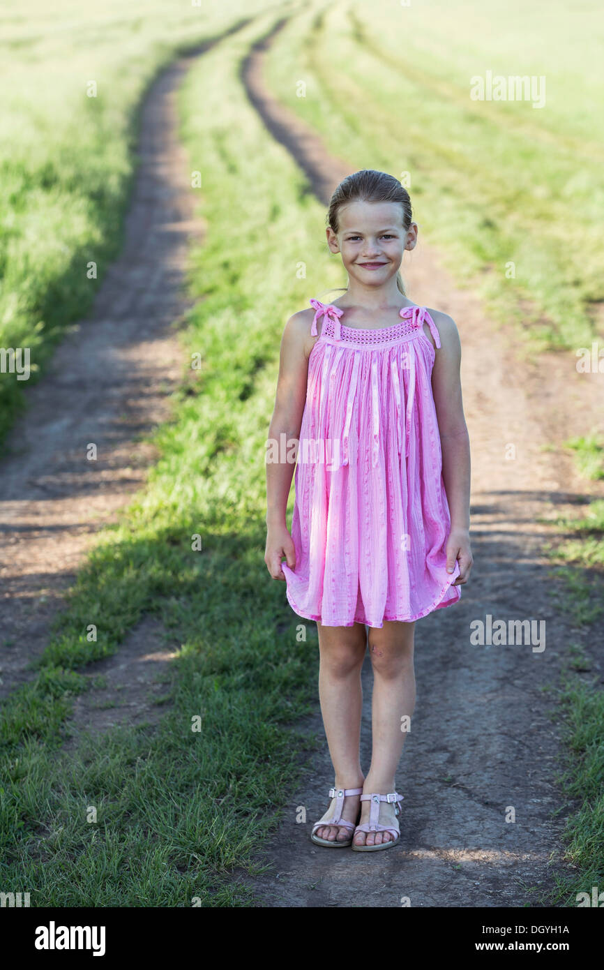 A young smiling girl standing on a dirt road in the country Stock Photo