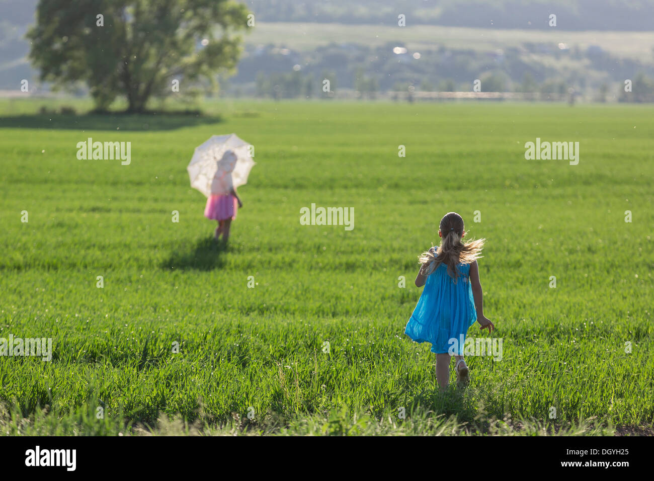 A young girl running to catch up with her twin sister in sunny field Stock Photo