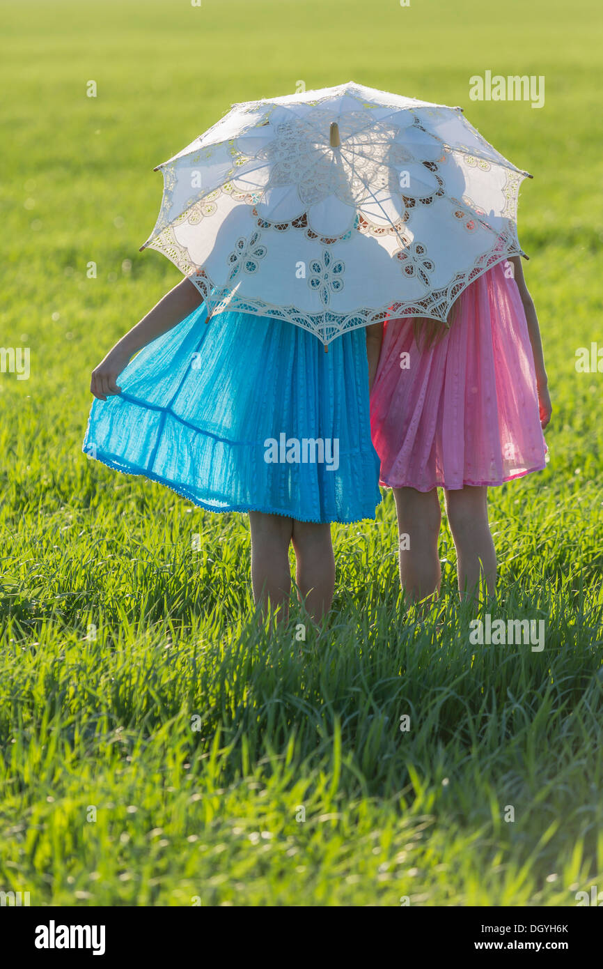 Twin sisters standing in a sunny field under an umbrella Stock Photo