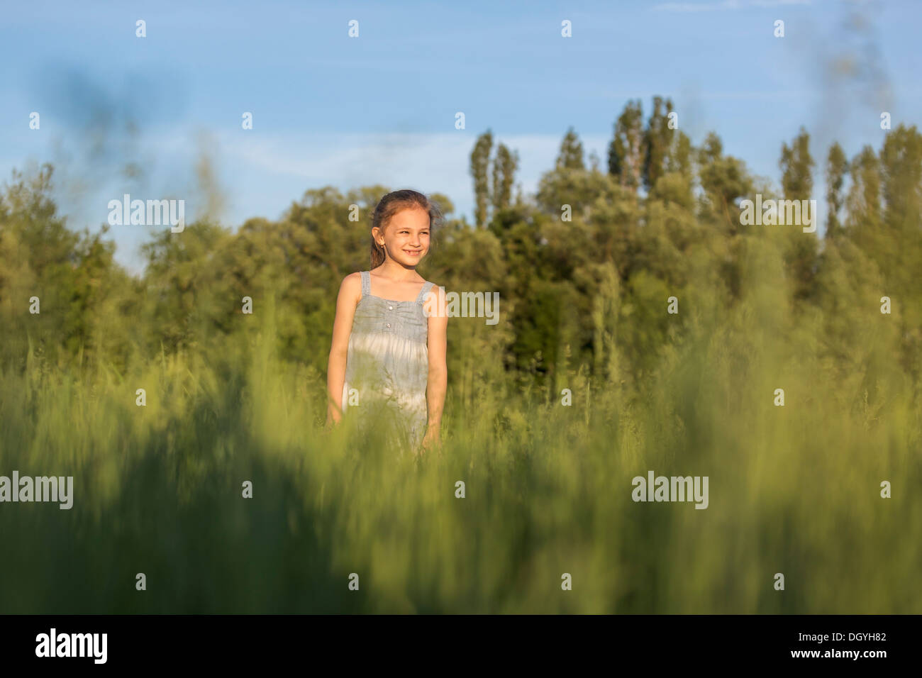 A young cheerful girl standing in a field looking at the view Stock Photo