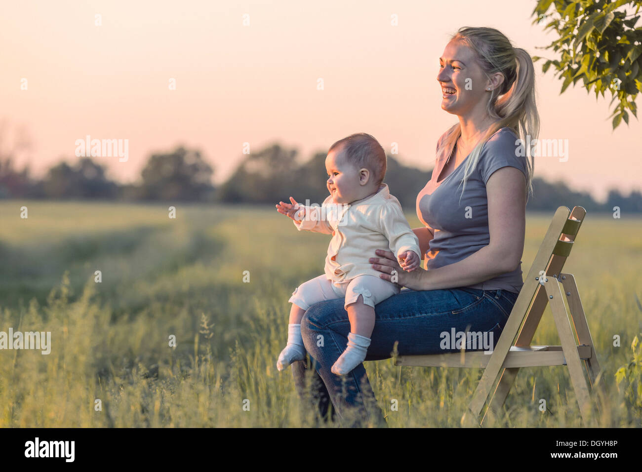 A laughing woman holding her baby while sitting on a chair in a field Stock Photo