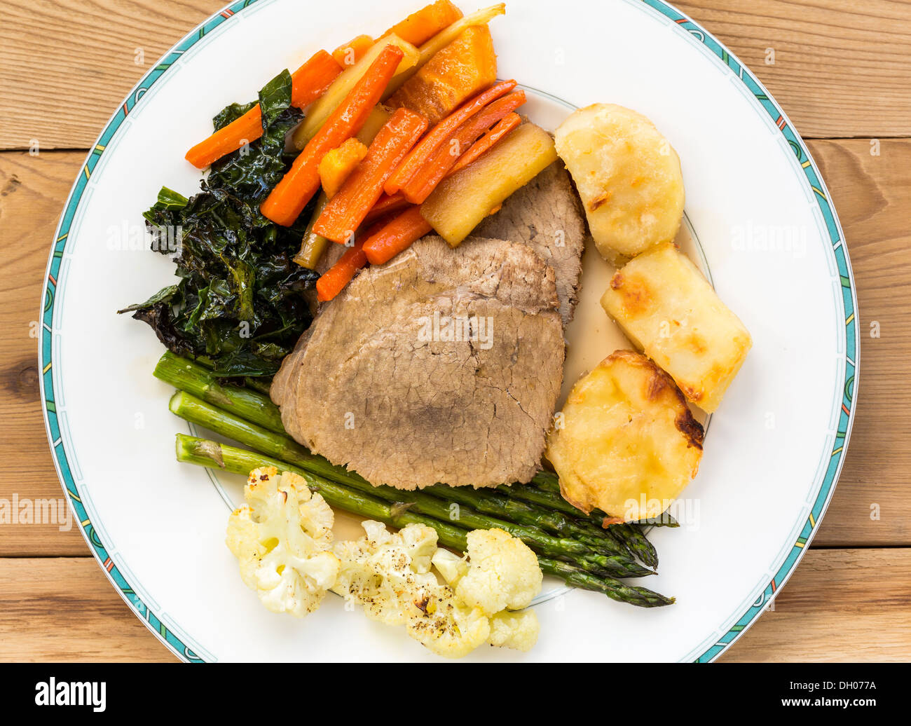Traditional British Sunday Lunch - roast beef, roasted potatoes, carrots, parsnips, kale, asparagus and cauliflower on a plate Stock Photo