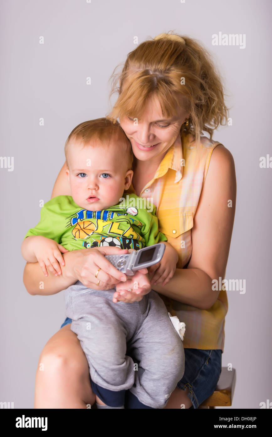 A boy between 1 and 2 years sitting on lap of a mature woman, a young grandmother, who is trying to initiate a cell phone call. Stock Photo