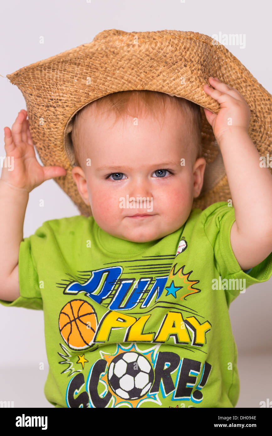 Male toddler child, 18 months old, caucasian ethnicity, is grabbing a straw cowboy hat he's wearing, which is way too large. Stock Photo