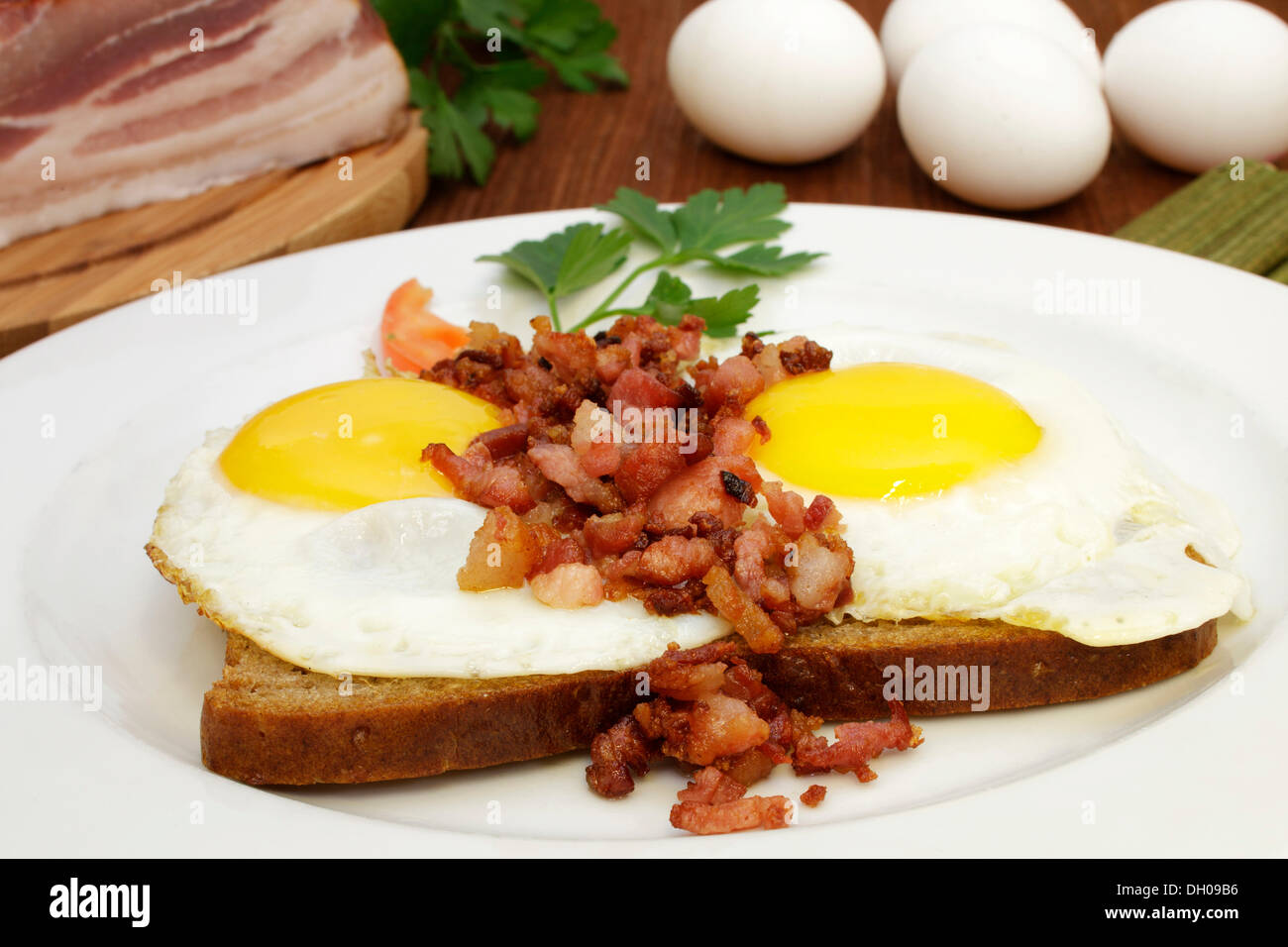 Fried eggs with fried bacon bits on bread, tomato slice, Italian