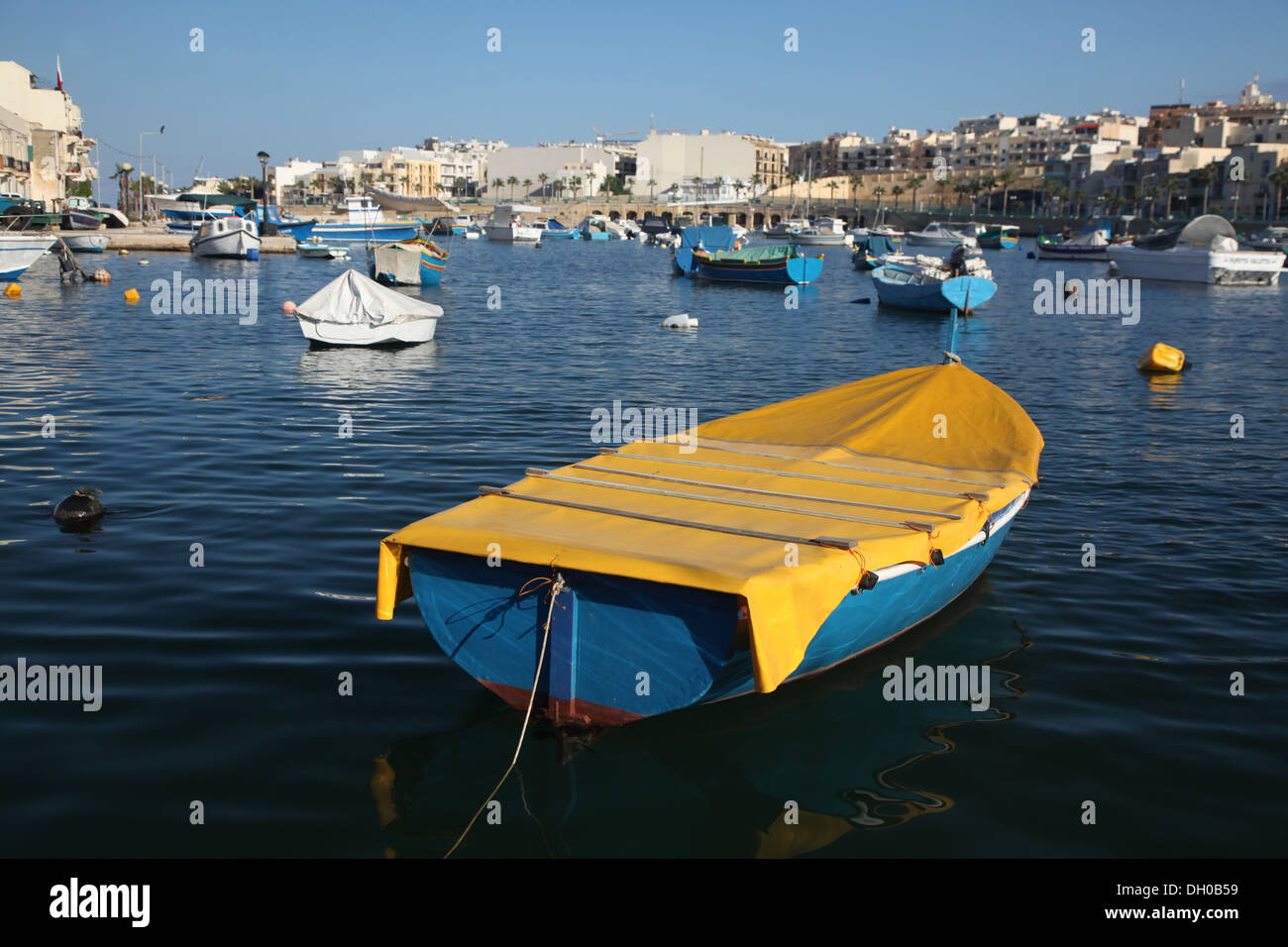 A neat yellow and blue dinghy moored in Marsascala's evening light Stock Photo