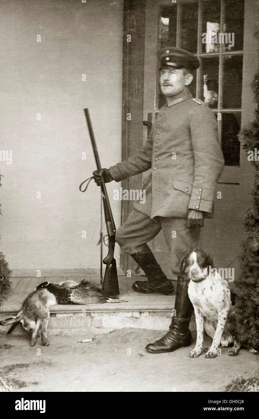 Hunter, a Prussian officer wearing his uniform holding a gun with a hunting dog, a shot hare and a shot pheasant lying next to Stock Photo