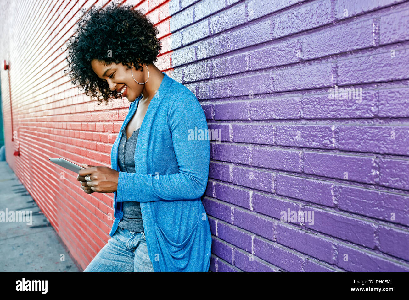 Mixed race woman with cell phone standing by colorful wall Stock Photo