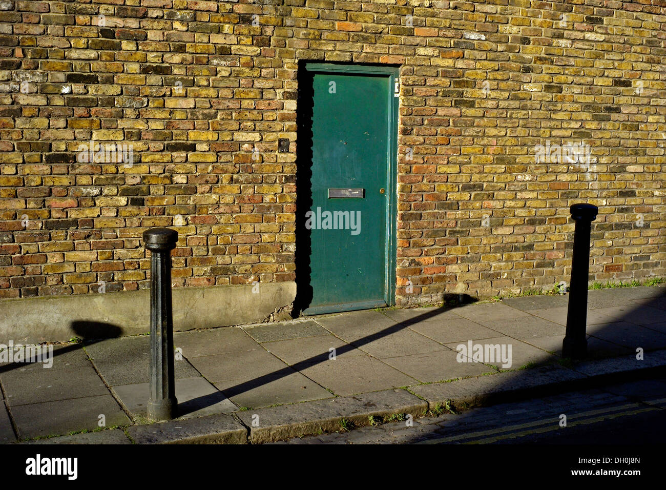 Green Door and brick wall Shadows of parking posts Camden Bollards across pavement Stock Photo