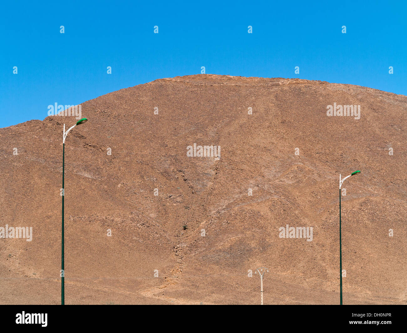 Three tall street lamps against a large rocky hill and blue sky Morocco Stock Photo