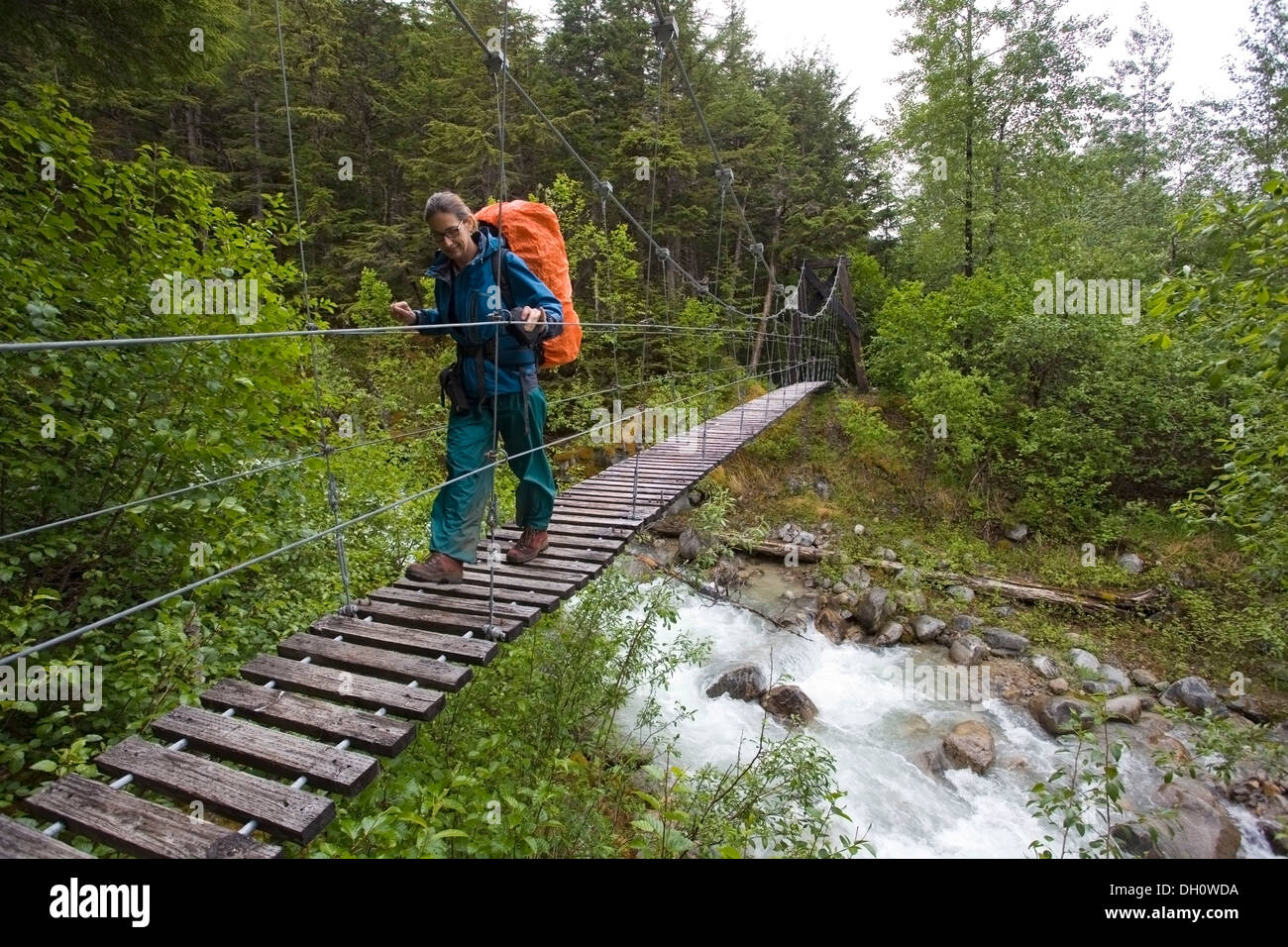 Woman, female hiker with backpack crossing suspension bridge across Taja River, near historic Canyon City, Pacific Northwest Stock Photo