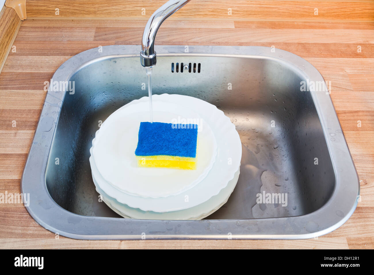 wash-up by cleaning sponge in metal washbasin in kitchen Stock Photo