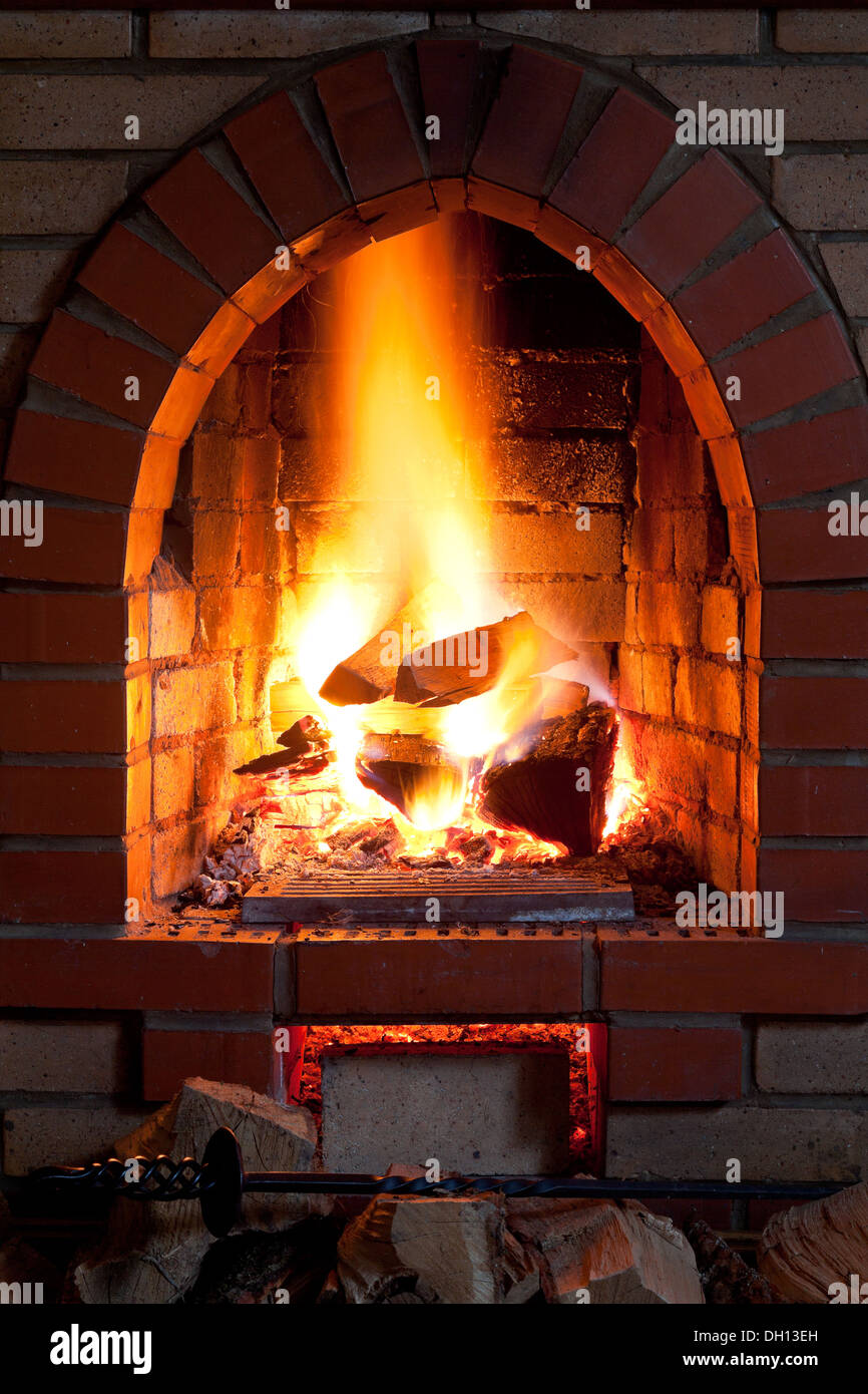 poker, firewood and flames of fire in fireplace in evening time Stock Photo