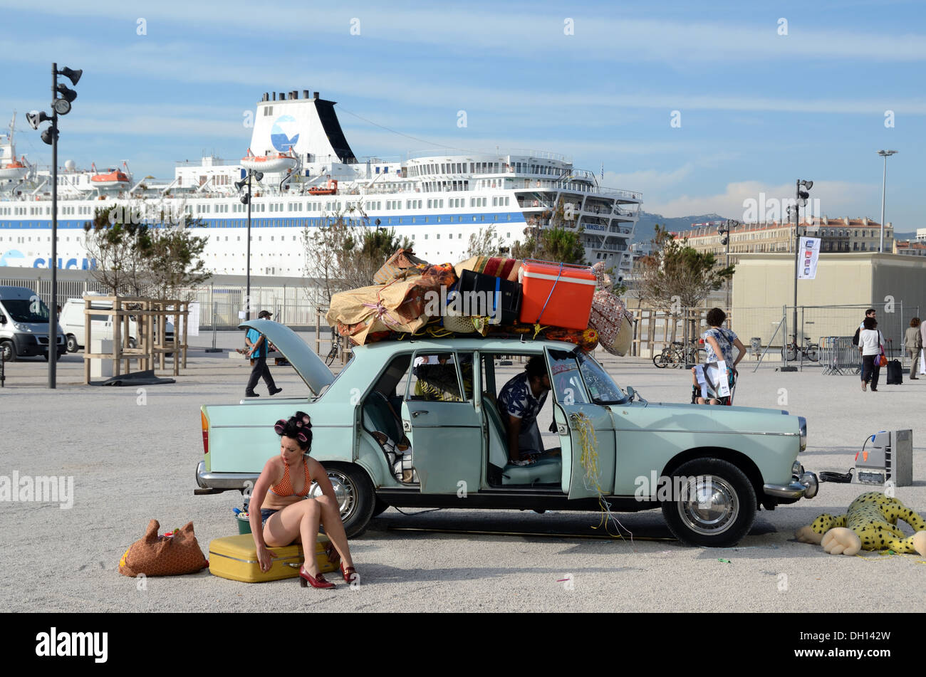 Female Tourist Packing Vintage Peugeot 204 Car, with Luggage & Bags on Overloaded Roof Rack, on the Waterfront with Ferry Boat Marseille France Stock Photo