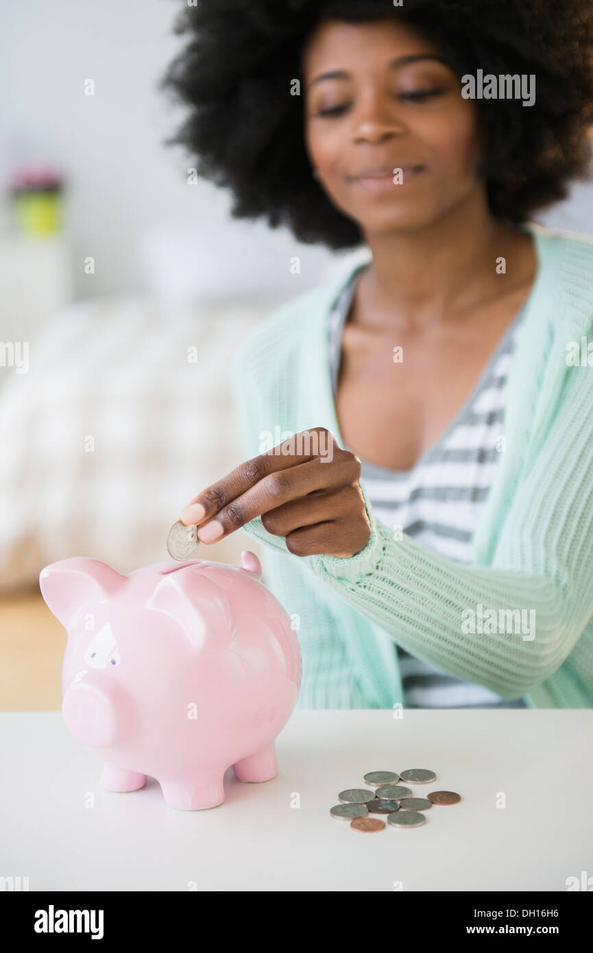 Mixed race woman putting coins in piggy bank Stock Photo