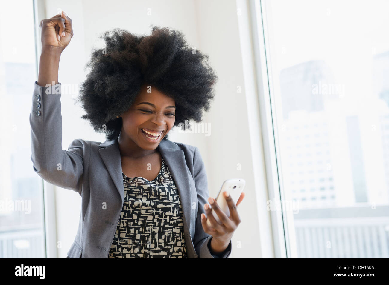 Mixed race businesswoman holding cell phone and cheering Stock Photo