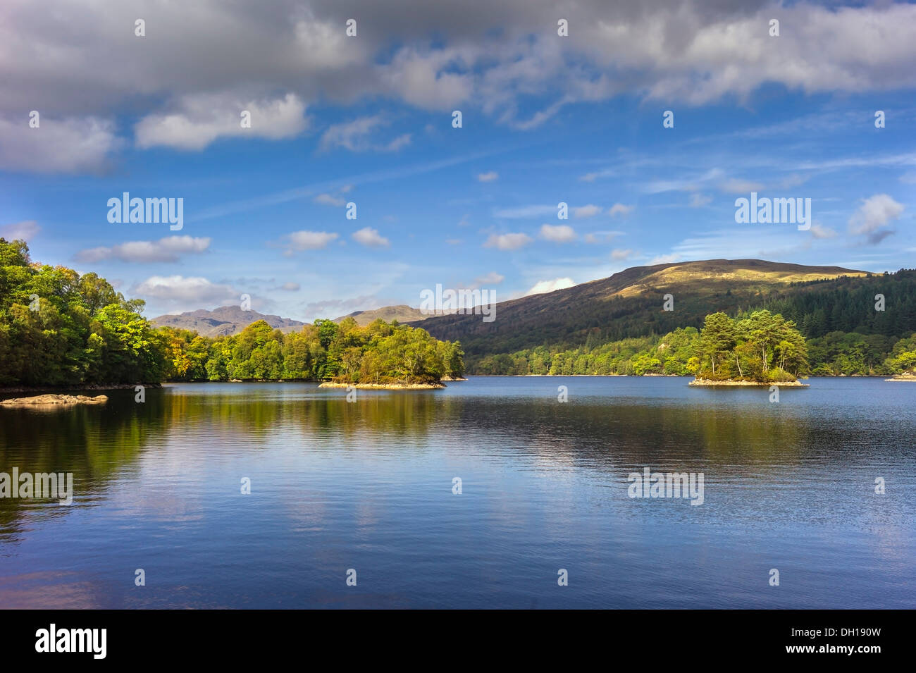 A view across the water of Loch Katrine in the Trossachs towards the highlands in the background, autumn sunlight and calm water Stock Photo