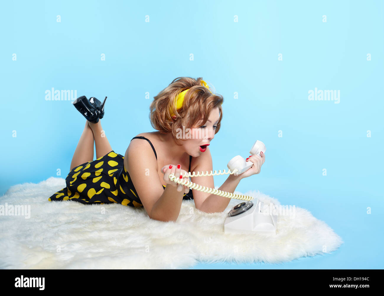 portrait of girl dressed and maked up in retro style posing on white fur with old-style telephone Stock Photo