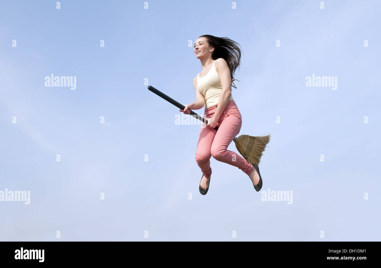 Energetic Asian woman wearing rubber gloves jumping in air with broom and l...