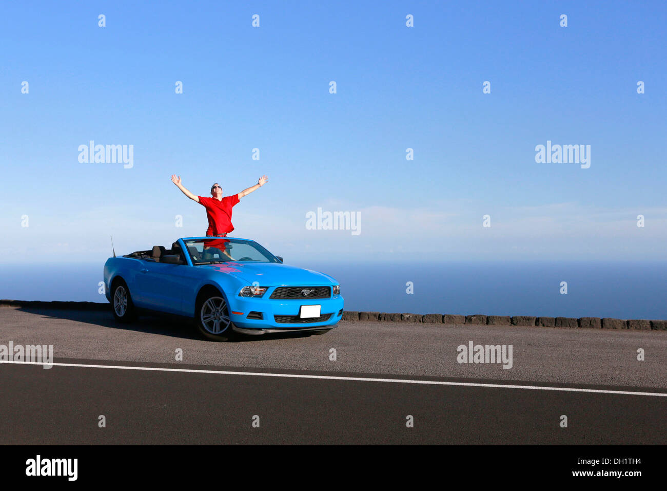 Happy man in a sky-blue Ford Mustang convertible by the sea, Big Island, Hawaii, USA Stock Photo