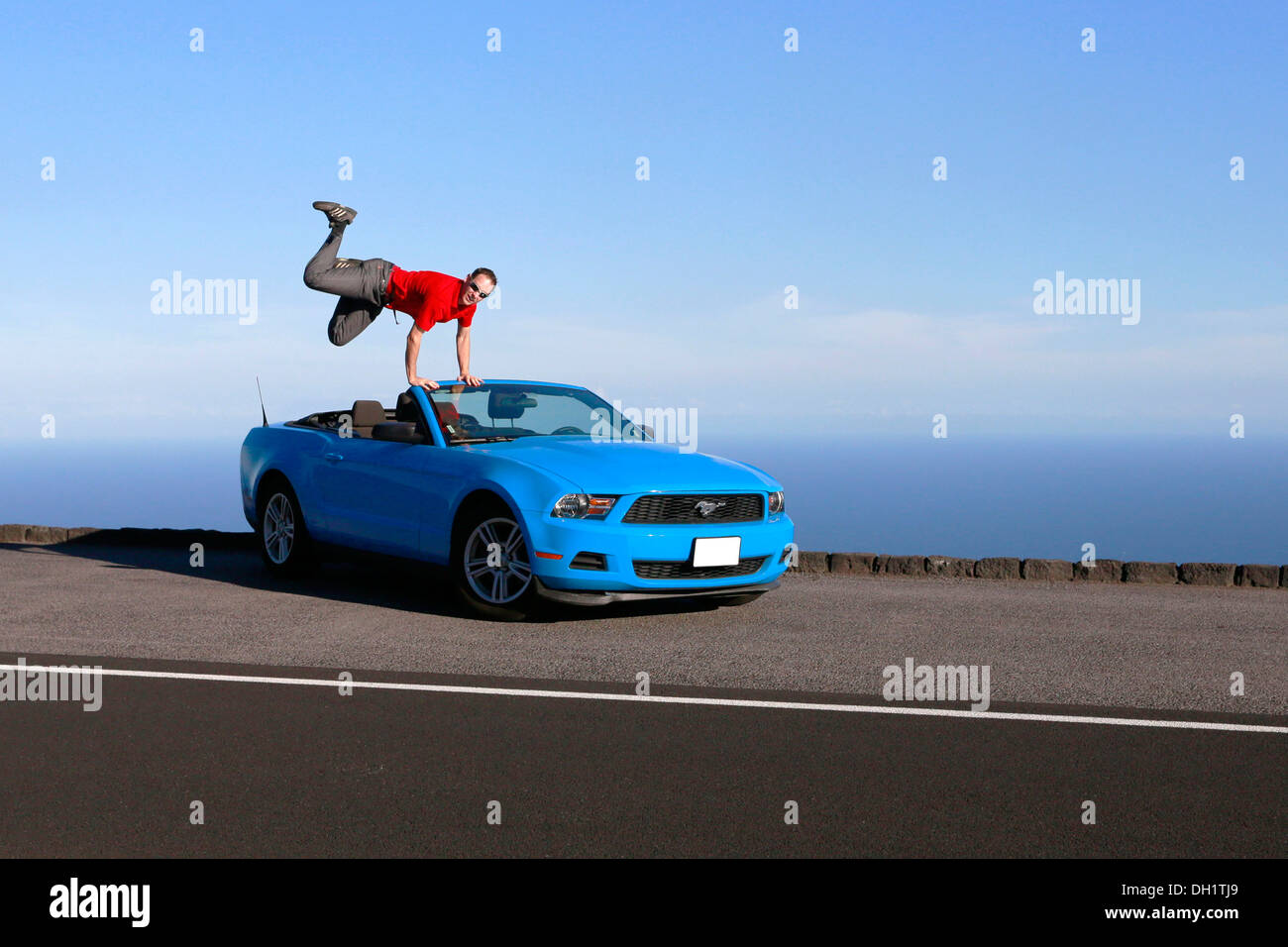 Man jumping with joy on a sky-blue Ford Mustang convertible by the sea, Big Island, Hawaii, USA Stock Photo