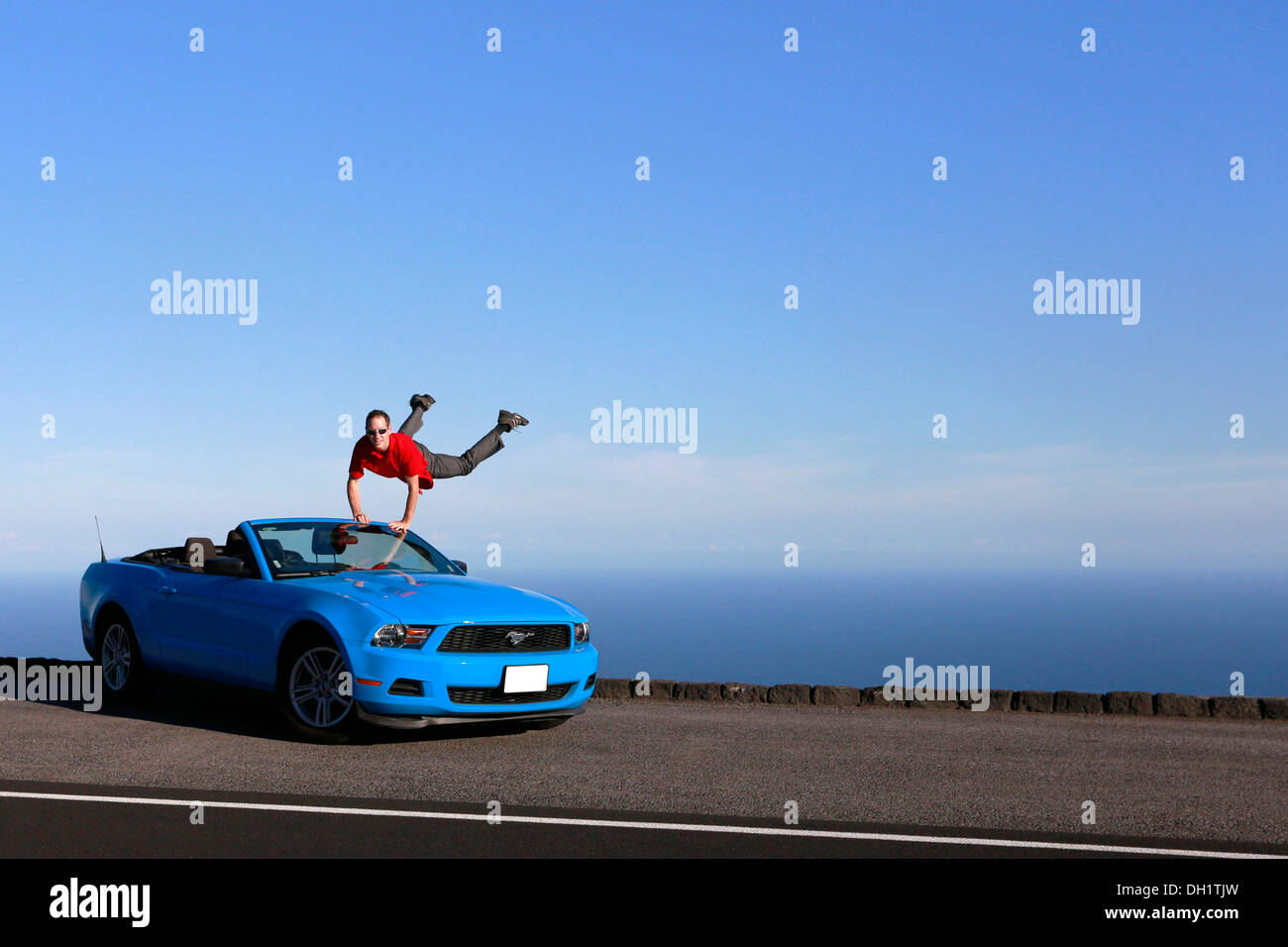 Man jumping with joy on a sky-blue Ford Mustang convertible by the sea, Big Island, Hawaii, USA Stock Photo