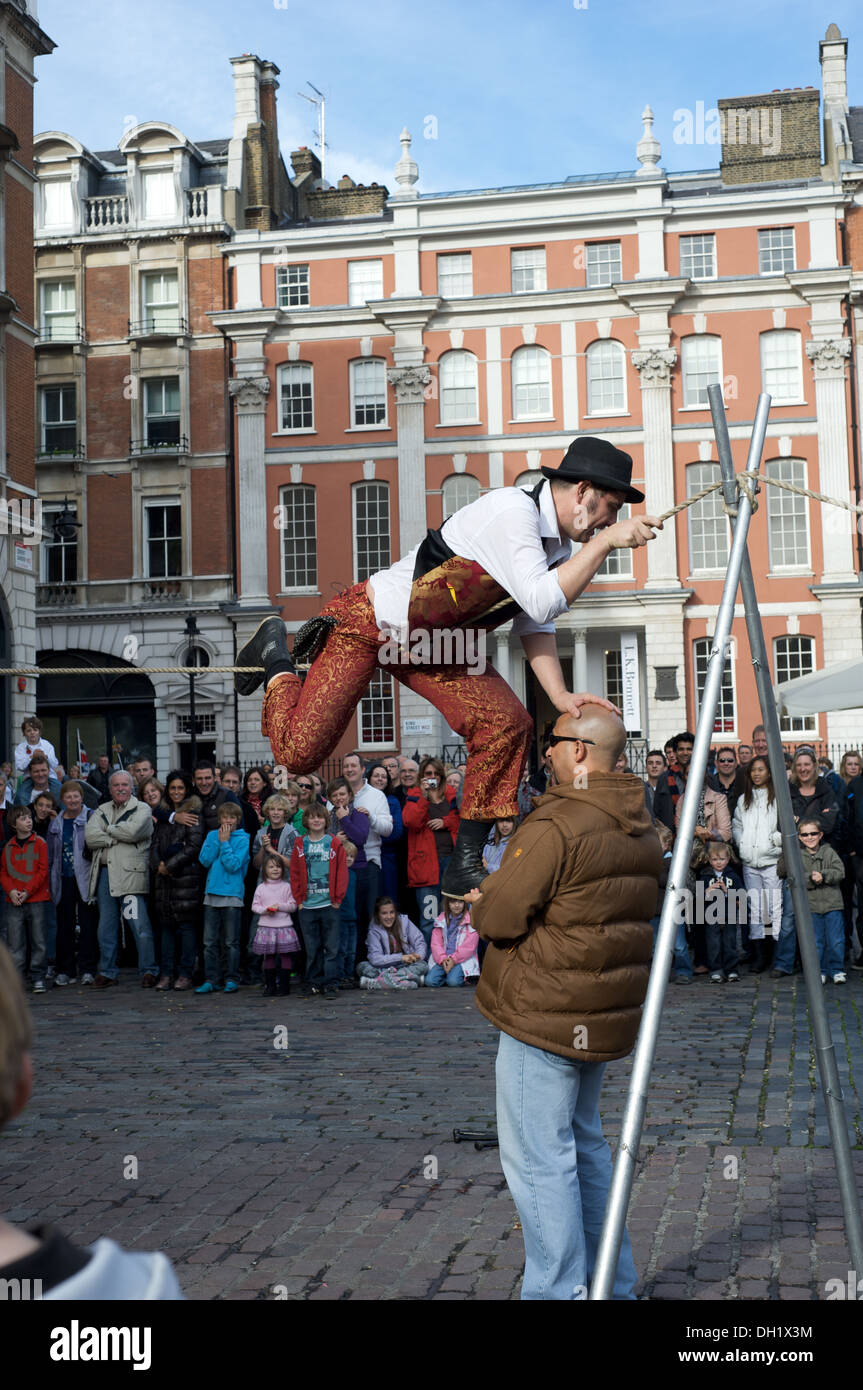 Street entertainer employs audience member to help with high wire act in Covent Garden, London, England Stock Photo