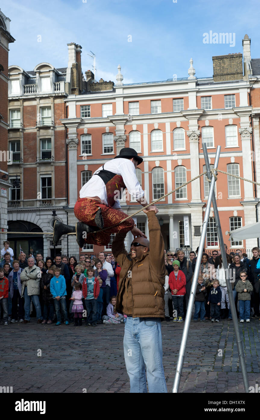 Member of the audience helps busker on highwire in Covent Garden, London, England Stock Photo