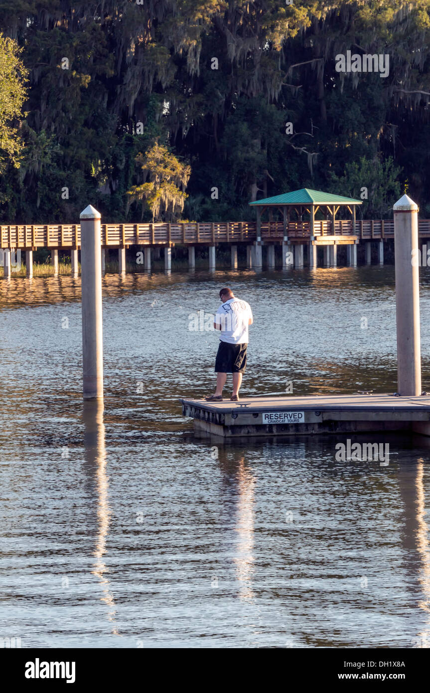 Man with fishing pole fishing from a dock in the Mount Dora harbor in  central Florida, nature trail boardwalk visible beyond Stock Photo - Alamy