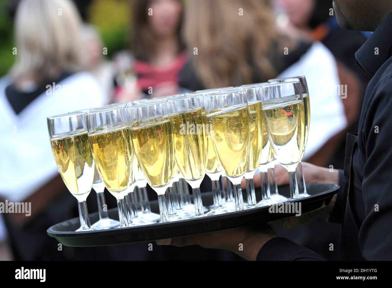 Black waiter carries a tray of champagne glasses at a graduation party Stock Photo