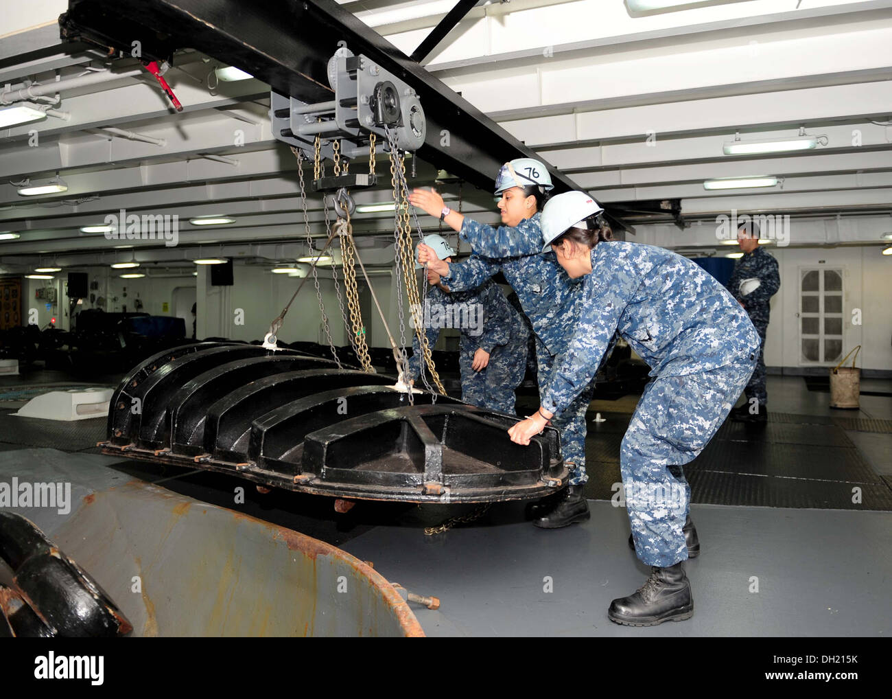 Sailors use a chain hoist to move a hawse pipe cover aboard the