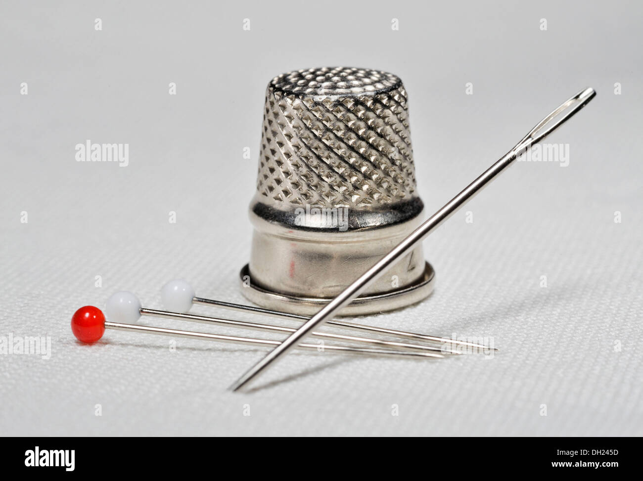 Sewing needle, pins and thimble lying on white linen fabric Stock Photo