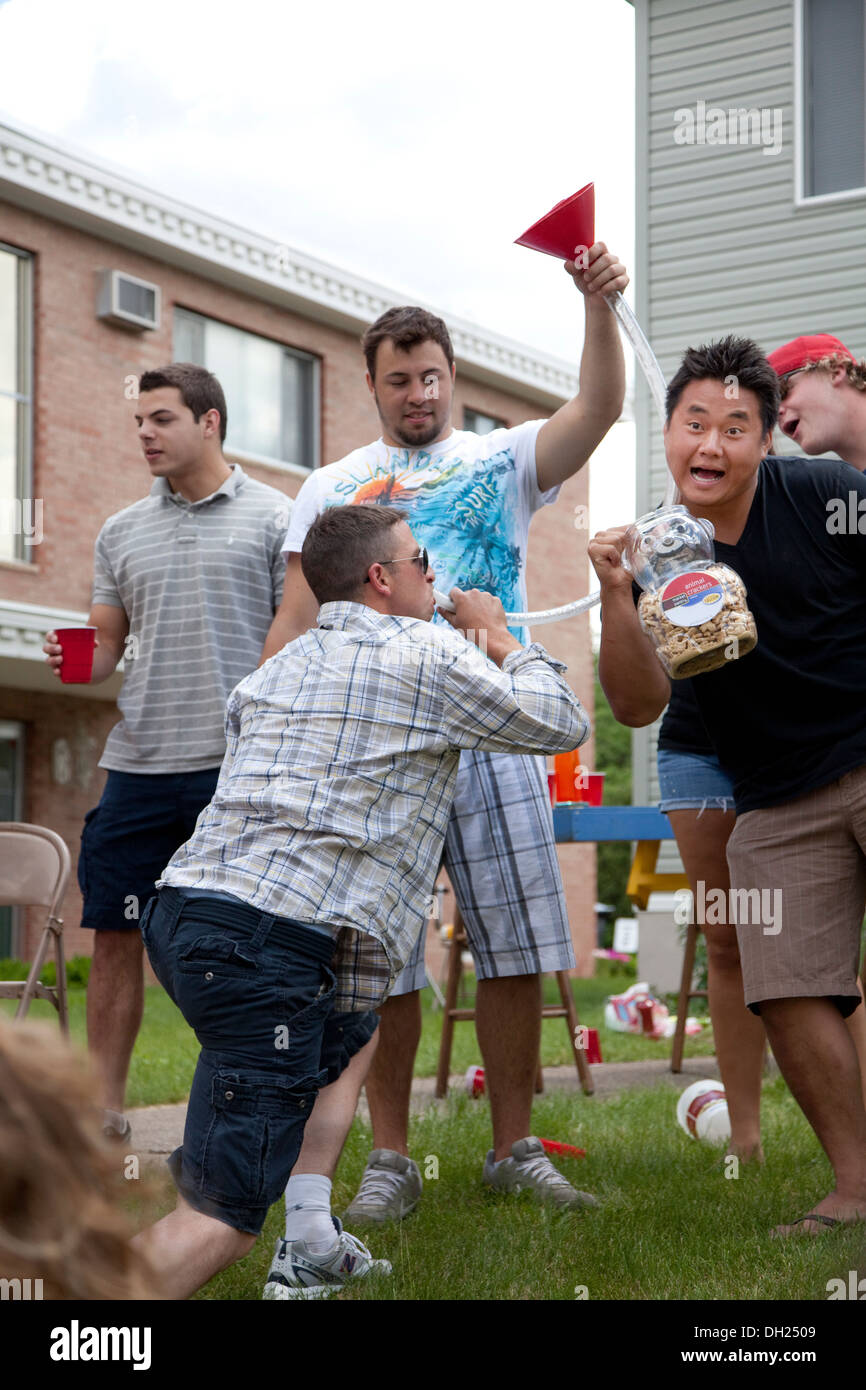 Boys having fun drinking from a beer bong a funnel with a hose. Grand