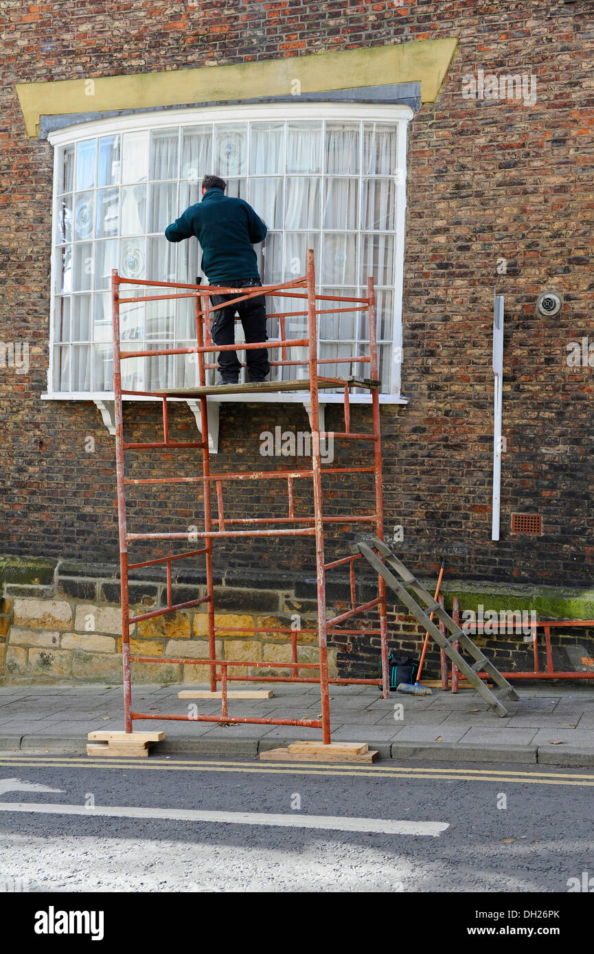 Trades man using a steel mobile scaffold supported by wooden blocks. Stock Photo