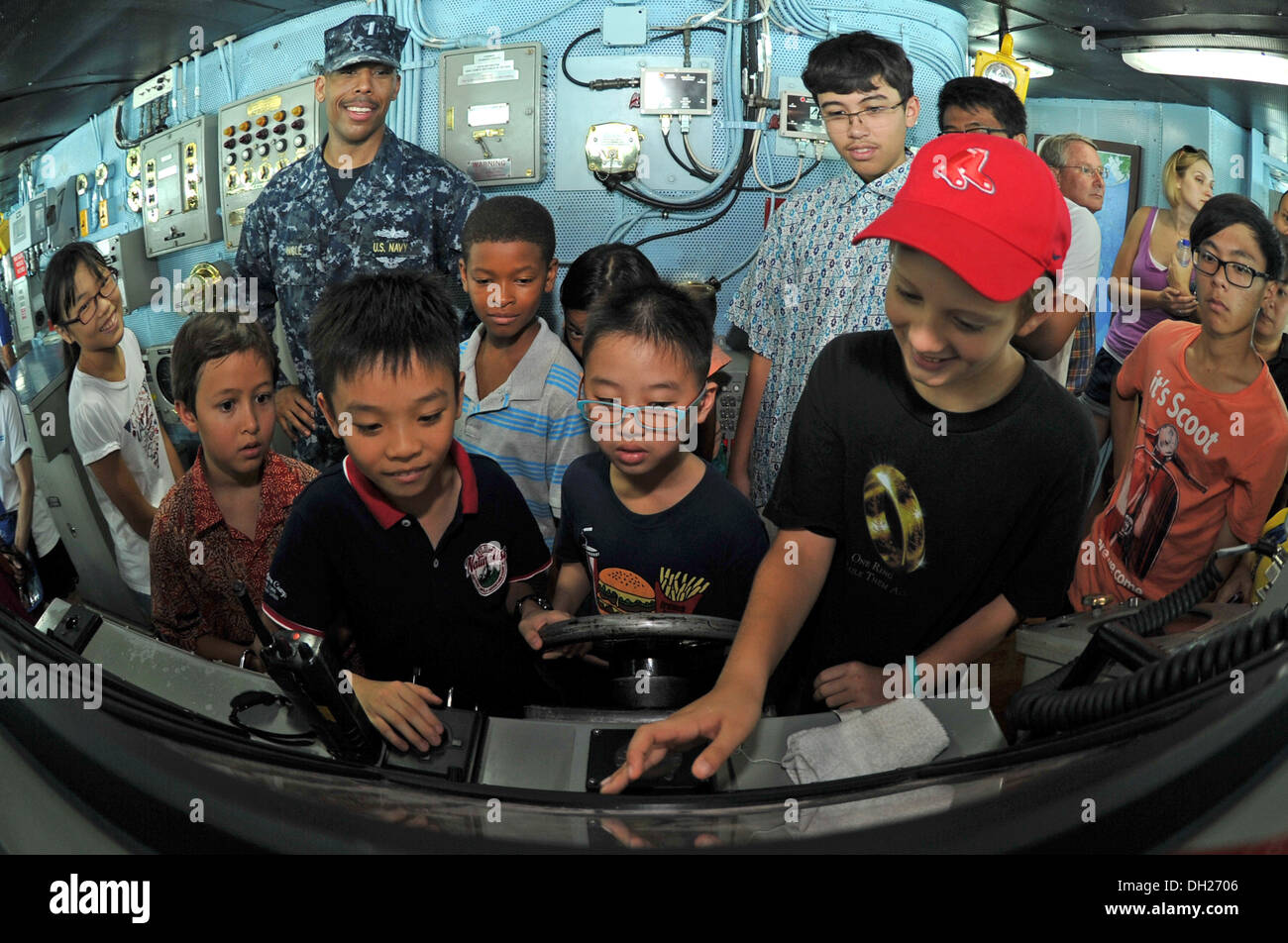 REPUBLIC OF SINGAPORE (Oct. 27, 2013) Lt. j.g. Derrick Ingle, top-left, assistant public affairs officer aboard the aircraft carrier USS George Washington (CVN 73), discusses the functions of the helm in the navigation bridge to children during a ship tou Stock Photo
