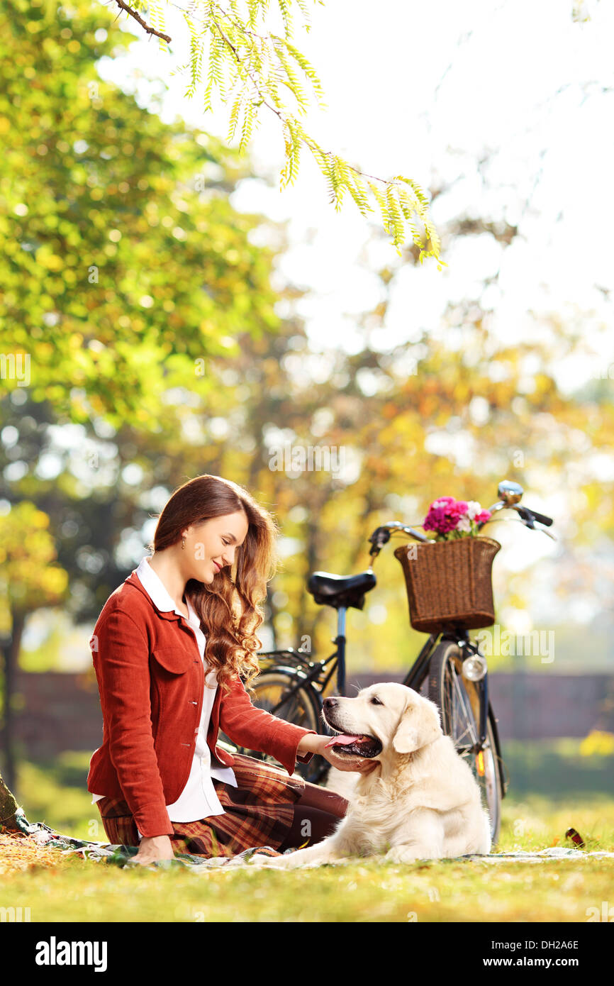 Beautiful female sitting on a grass and looking at her dog in a park ...