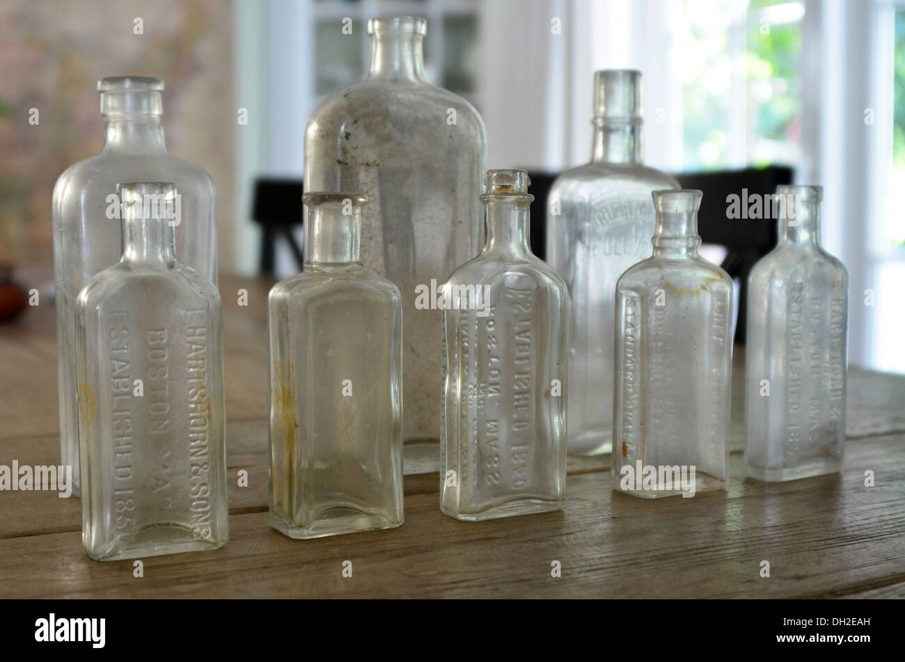 Antique bottles lined up on a wooden dining table with a window in the distance. Stock Photo