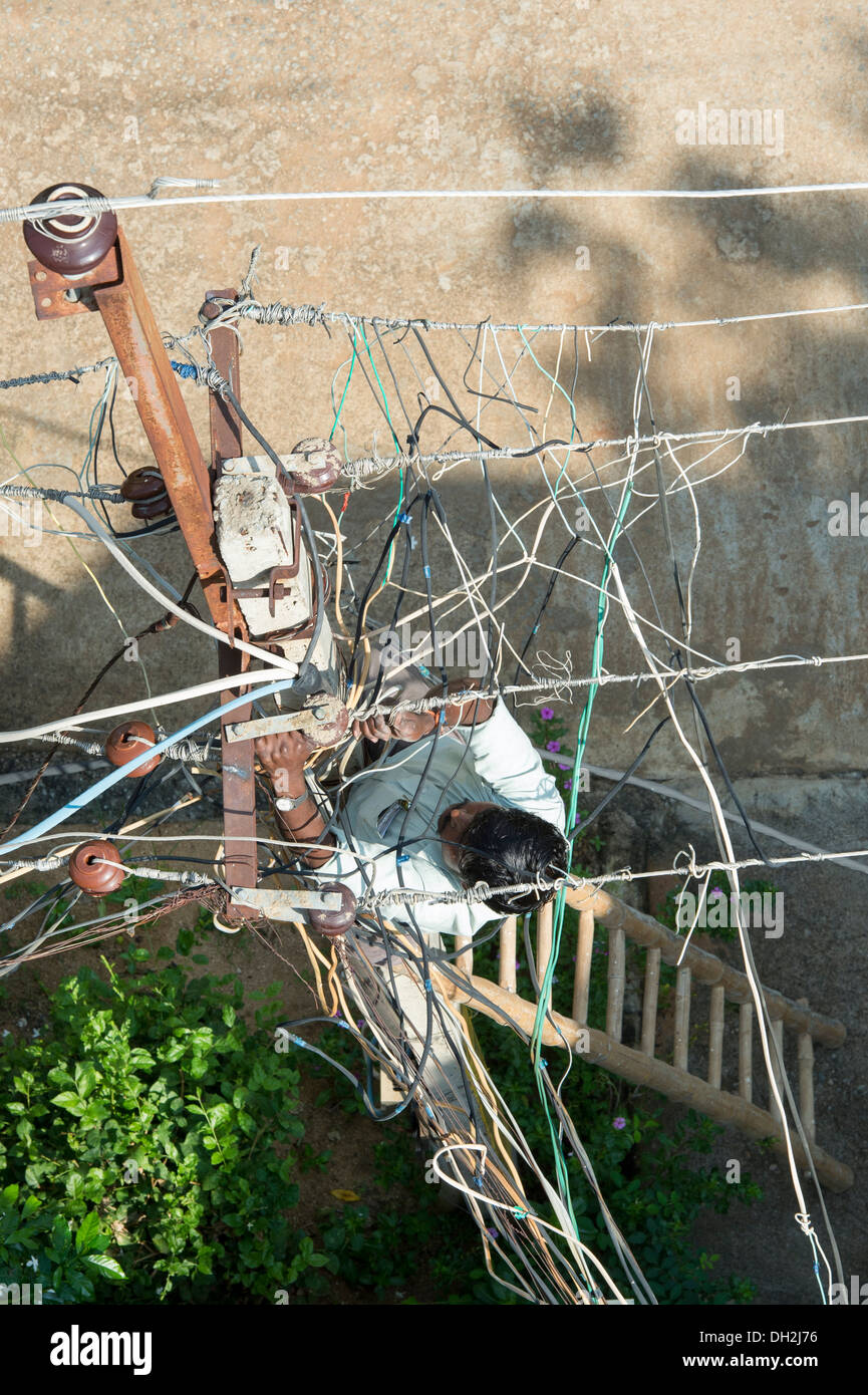 Looking down on an Indian Electrician working up an Electricity pylon in the streets of Puttaparthi, Andhra Pradesh, India Stock Photo