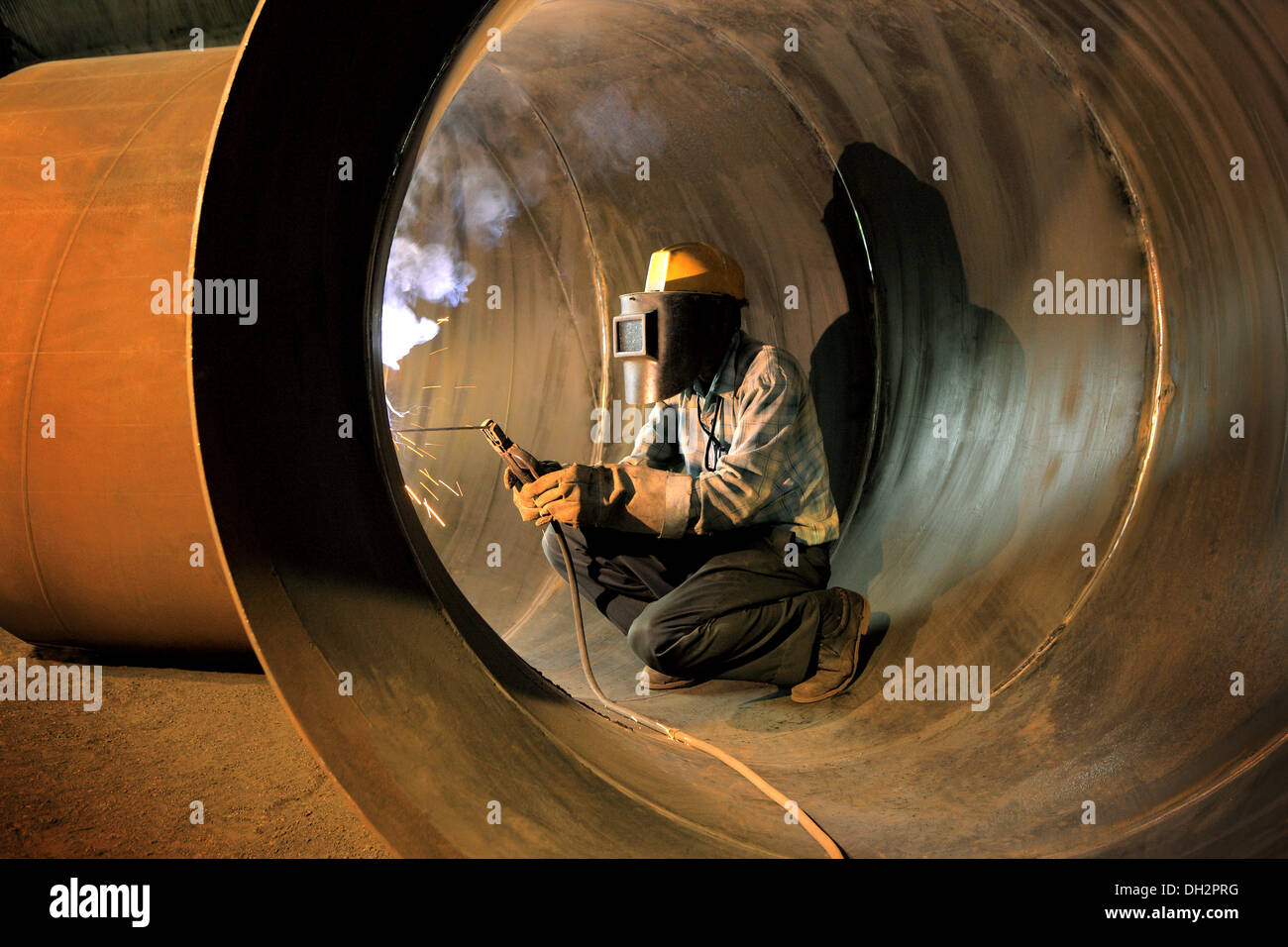 Industrial worker welding with safety gear in industrial pipe Stock Photo