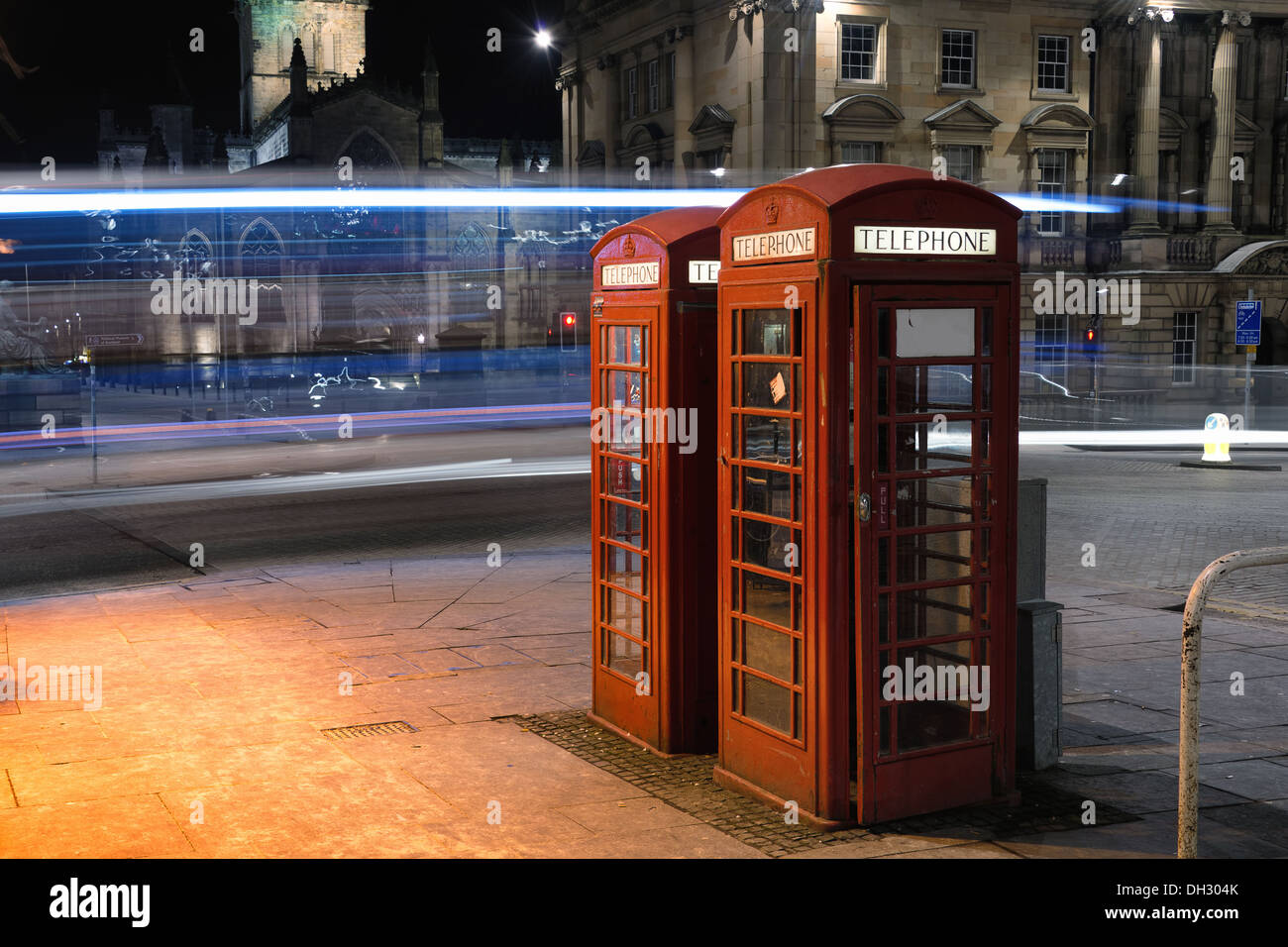 Red telephone boxes in Edinburgh, a bus leaving light trails on the background. Stock Photo