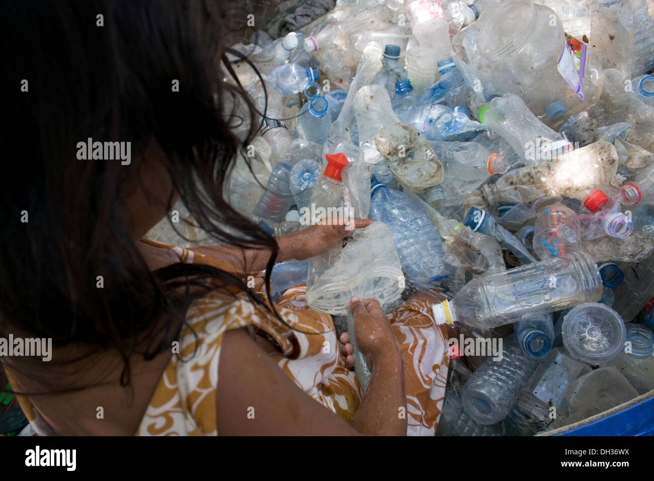 A young girl is sitting in a tub crushing plastic water bottles at a recycling depot in Phnom