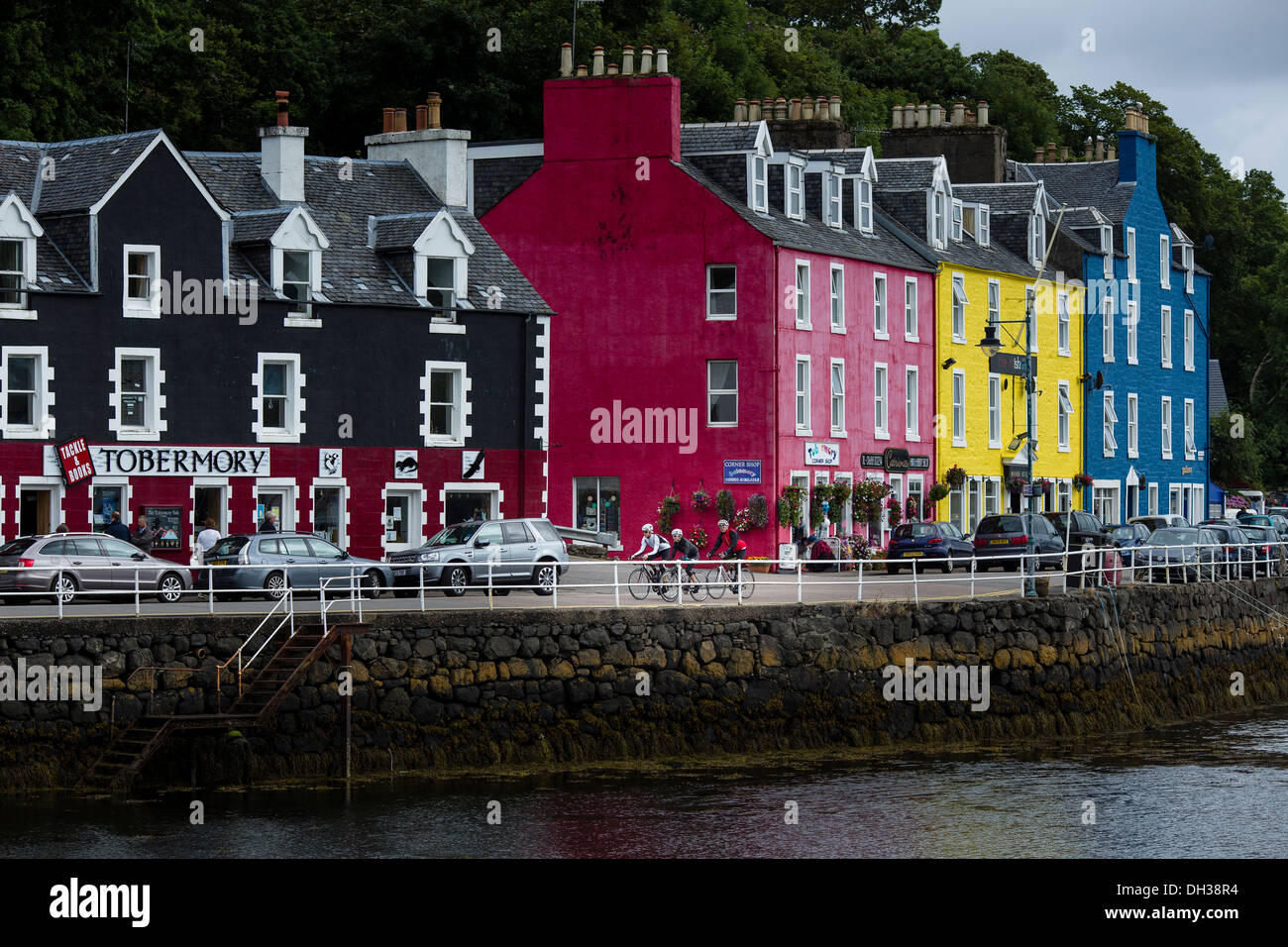 Cyclists ride by colourful buildings in the Scottish Highlands, Scotland, United Kingdom Stock Photo