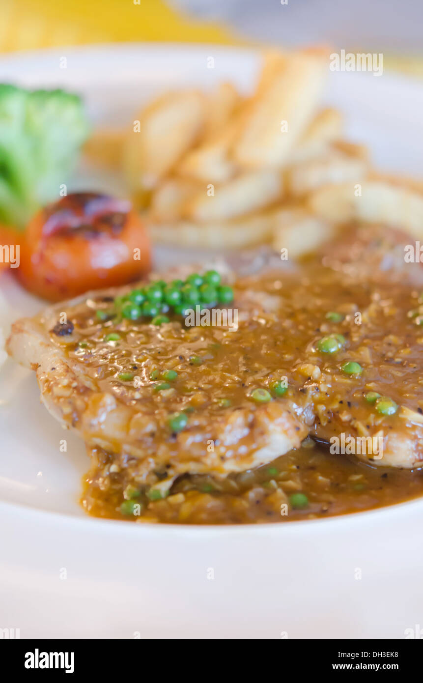 close up beef steak with green peppercorn sauce served with chips and