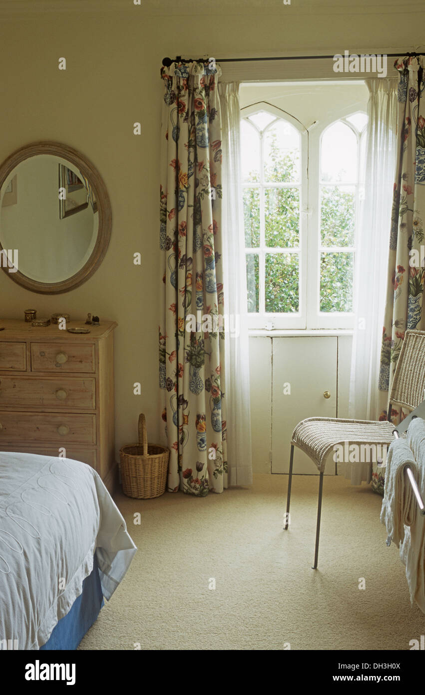 Floral curtains at arched window in country bedroom with oval mirror and cream carpet Stock Photo